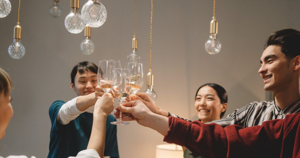 Group of young friends toasting with wine glasses, celebrating indoors under warm lighting.