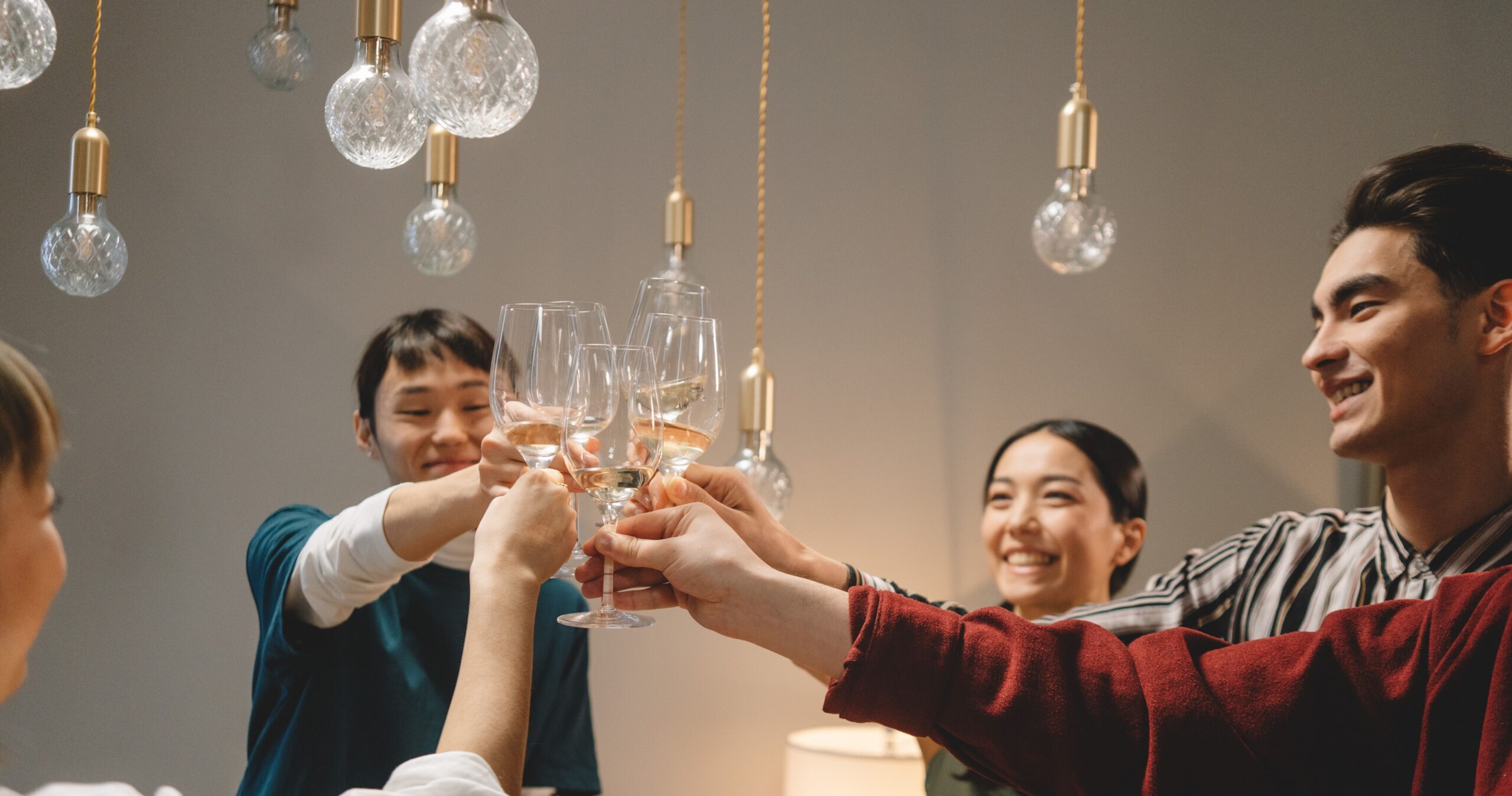 Group of young friends toasting with wine glasses, celebrating indoors under warm lighting.